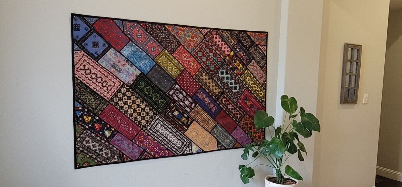 Colorful patchwork quilt hanging on a wall next to a plant